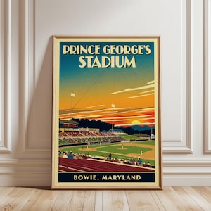 May include: A framed poster featuring a stylized illustration of Prince George's Stadium in Bowie, Maryland. The artwork depicts a baseball field at sunset with orange and blue skies, stadium lights, and spectators in the stands.