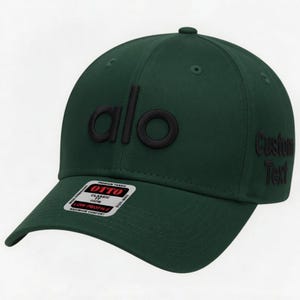 Pu&ograve; includere: Un cappellino da baseball verde scuro con la scritta "alo" in nero in rilievo sul davanti. Il lato destro del cappellino riporta le parole "Custom Text" in nero. Il cappellino ha una visiera curva e una piccola etichetta con "OTTO" e "Classic".