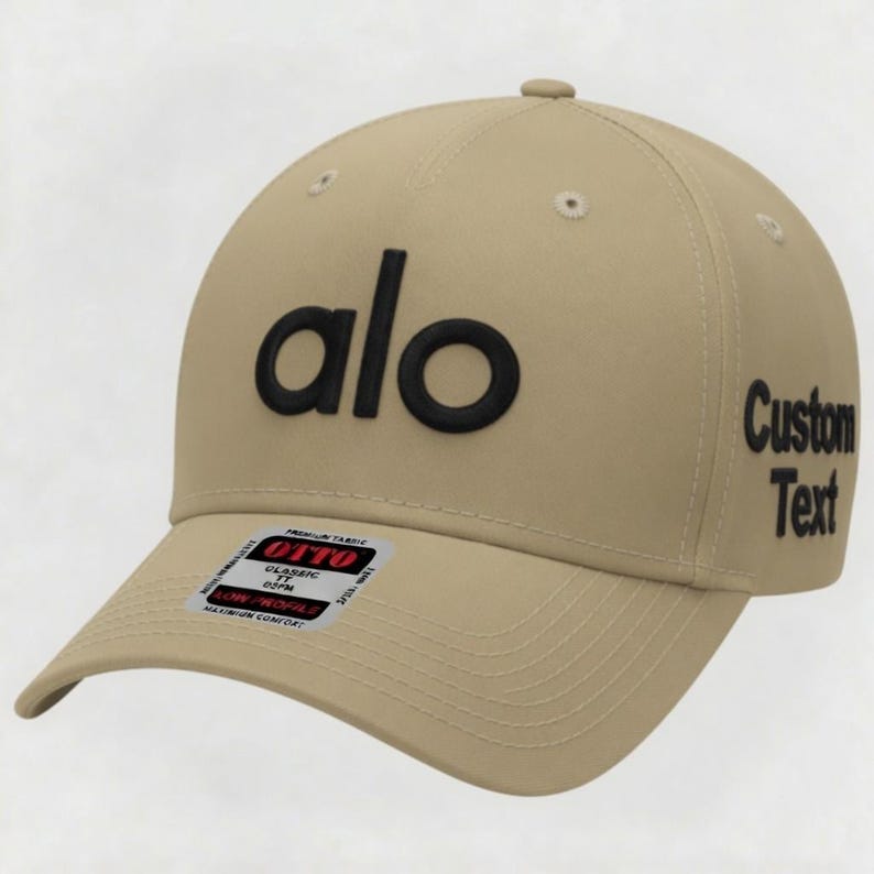 Pu&ograve; includere: Cappellino da baseball beige con la scritta "alo" in lettere nere sul davanti. Il lato destro del cappellino riporta le parole "Custom Text" in nero. Un piccolo adesivo &egrave; sulla visiera.