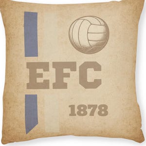 Könnte beinhalten: Quadratisches Kissen mit Vintage-Design. Das Kissen zeigt eine Volleyball-Grafik, die Buchstaben "EFC" und das Jahr "1878" in einem Used-Look. Auf der linken Seite des Kissens befinden sich zwei vertikale blaue Streifen.
