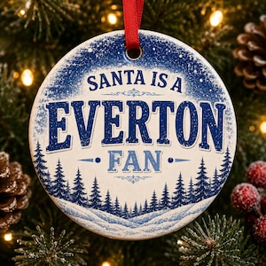 May include: A round ceramic Christmas ornament with a red ribbon hanger. The design features a snowy landscape with dark blue pine trees at the bottom and a starry sky at the top. The text reads SANTA IS A EVERTON FAN in blue lettering.