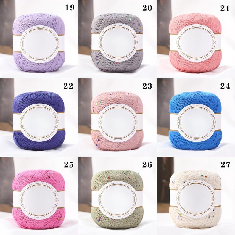 Puede incluir: Una colecci&oacute;n de nueve madejas de hilo en varios colores, incluyendo lavanda, gris, rosa, azul y verde. Cada madeja tiene una etiqueta blanca con un dise&ntilde;o ovalado. El hilo parece tener una textura moteada, con peque&ntilde;os adornos coloridos.