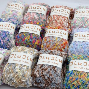 May include: A selection of multi-coloured yarn skeins, each with a label reading "Jiu Jiu Hand Made". The yarn features a textured appearance in shades of blue, pink, orange, brown, and yellow, creating a visually appealing arrangement.