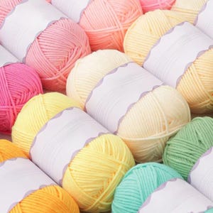Può includere: Una collezione di gomitoli di filato in vari colori pastello, tra cui rosa, giallo e verde. Ogni gomitolo è avvolto con un'etichetta bianca. Il filato appare morbido e soffice, adatto per progetti di maglieria o uncinetto.