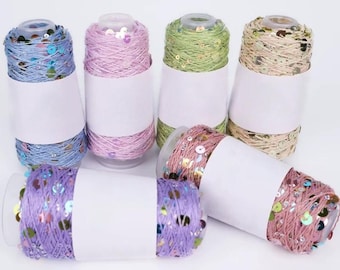 May include: Spools of colorful yarn with sequins in various shades, including blue, pink, green, and gold. Each spool is wrapped with a white label. The yarn is likely used for crafting and sewing projects.