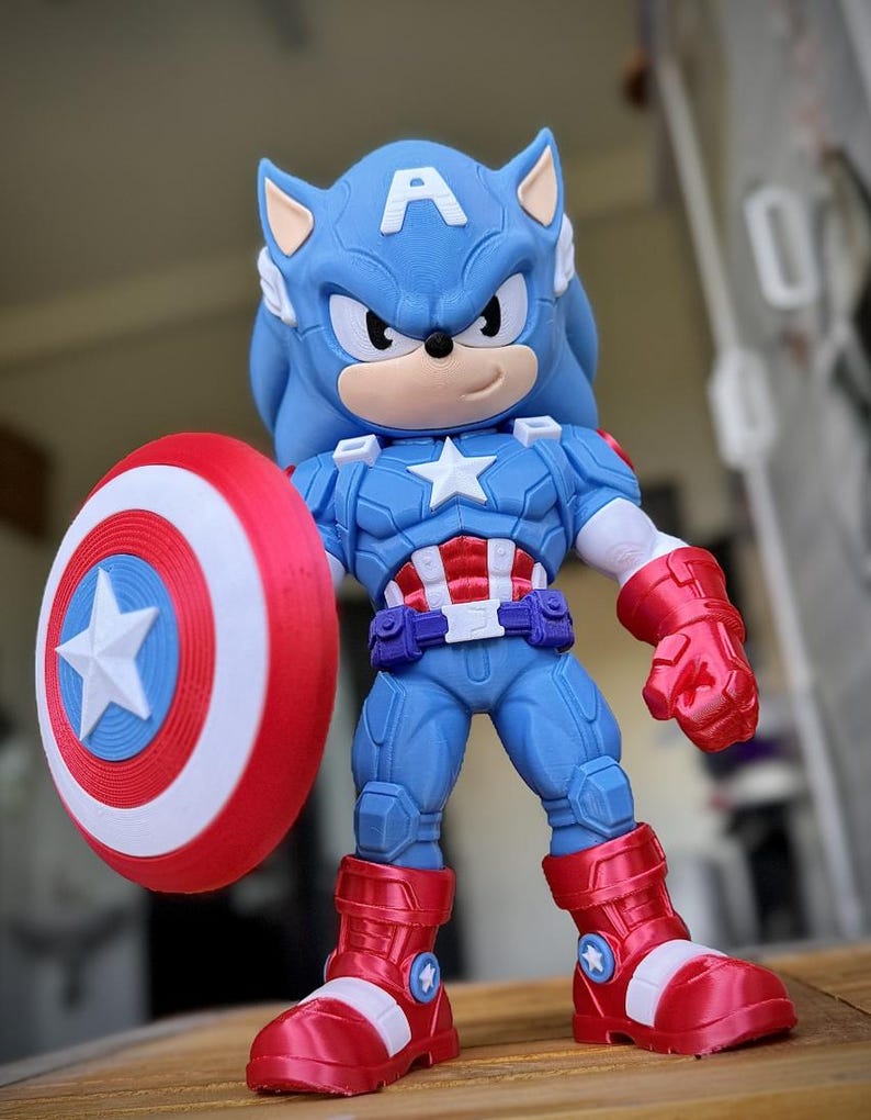 Op de afbeelding: Een blauw en rood actiefiguur van een Sonic the Hedgehog-Captain America hybride. Het figuur houdt een rood, wit en blauw schild vast. Het figuur draagt een blauw pak met een witte ster en rode laarzen.