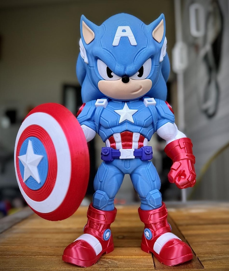Op de afbeelding: Een blauw en rood beeldje van Sonic the Hedgehog verkleed als Captain America, met een schild. Het beeldje heeft een blauw lichaam, rode laarzen en handschoenen en een witte ster op de borst. Het schild is rood, wit en blauw.