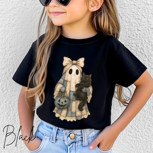 Puede incluir: Una camiseta negra de manga corta con el gráfico de un fantasma que lleva un gran lazo beige y un vestido con estampado azul. El fantasma sostiene un pequeño cubo de calabaza naranja en una mano y lleva un gato negro esponjoso en el brazo.