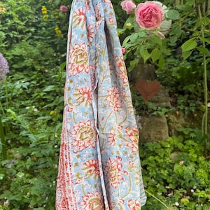 Könnte beinhalten: Ein rechteckiger Schal mit hellblauem Hintergrund und einem sich wiederholenden Blumenmuster in Rot-, Orange- und Grüntönen. Der Stoff zeigt einen dekorativen Rand mit einem roten, vom Paisley-Muster inspirierten Design und einem hellblauen Zickzackmuster.