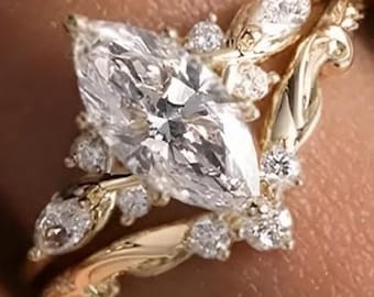 May include: A gold ring set featuring a central marquise-cut diamond flanked by smaller marquise and round-cut diamonds. The band has a curved, organic shape with intricate metal detailing, creating a layered appearance with multiple sparkling stones.