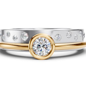 May include: A two-tone ring with a gold band and a silver top band. The silver band has small, evenly spaced diamonds. The center of the ring features a larger diamond set in a gold bezel.