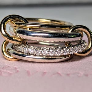 May include: A stack of rings with a gold and silver design. The top and bottom rings are gold, with a silver ring in the middle. The bottom silver ring is encrusted with small, clear stones. The rings are interlocked.
