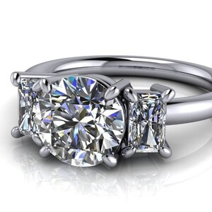 Pu&ograve; includere: Un anello di fidanzamento in argento a tre pietre con una grande pietra centrale rotonda e due pietre rettangolari pi&ugrave; piccole su entrambi i lati.