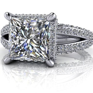 May include: A square-shaped diamond engagement ring with a halo setting and a split shank. The ring is set in white gold and features a row of small diamonds on each side of the center stone.
