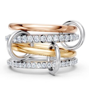 May include: A multi-tone ring set featuring a rose gold band, a gold band, and two silver bands, one of which is encrusted with small, sparkling stones. The rings are interlocked with silver hoops.