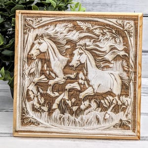 May include: A square wooden carving featuring two running horses. The horses are carved in a light color against a darker wood background, surrounded by foliage. The carving is framed with a light-colored border.