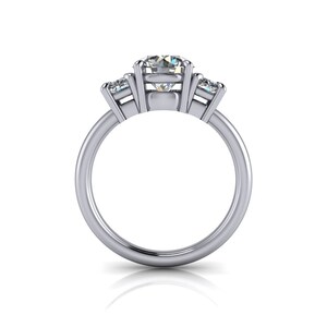 Pu&ograve; includere: Un anello di fidanzamento in argento a tre pietre con una grande pietra centrale rotonda e due pietre pi&ugrave; piccole a forma di pera su entrambi i lati.