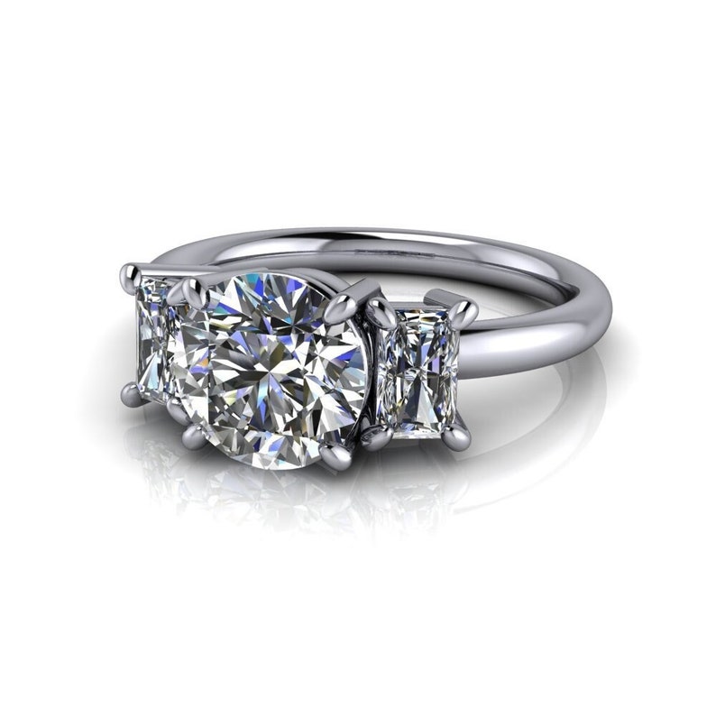 Pu&ograve; includere: Un anello di fidanzamento in argento a tre pietre con una grande pietra centrale rotonda e due pietre rettangolari pi&ugrave; piccole su entrambi i lati.