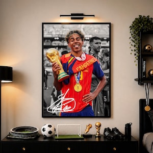 May include: A framed poster featuring a football player in a red jersey holding a gold trophy, wearing a gold medal, and a sash with the text CAMPEDNES. The image includes a white signature overlay on the lower portion of the player's red jersey.