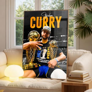 May include: A framed poster featuring Stephen Curry, with the word "CURRY" in large orange letters. Curry is holding two golden trophies, wearing a black t-shirt with "GOLDEN STATE WARRIORS" and a basketball graphic. He is also wearing a baseball cap.