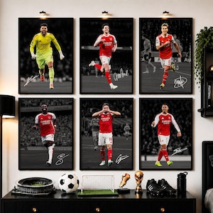May include: Six framed posters featuring Arsenal football players in action, each with a signature. The top row shows players in yellow and red kits, while the bottom row displays players in red and white kits, all set against a black and white background.