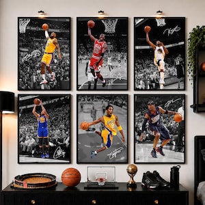 May include: A gallery wall set of six framed basketball posters featuring iconic players in action, including LeBron James, Michael Jordan, Stephen Curry, and Kobe Bryant, with signatures on each print, displayed above a black console table.