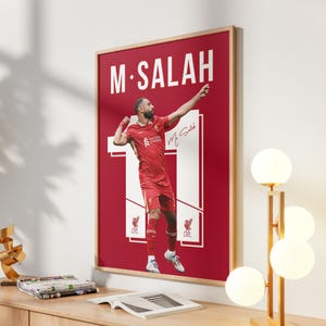 May include: Framed poster featuring soccer player M. Salah in a red uniform, with the number 11. The poster has a red background with white text and a signature. The image is in a wooden frame.