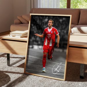 May include: A framed vertical poster featuring a color photograph of a soccer player in a red and white jersey with the letter T on the chest, running on a field. The background is black and white, and a white signature is visible in the corner.