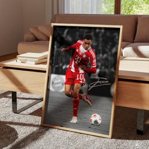 May include: A framed vertical poster featuring a color photograph of a soccer player in a red and white jersey with the number 10, dribbling a soccer ball on a field, set against a black and white background with a white signature overlay.