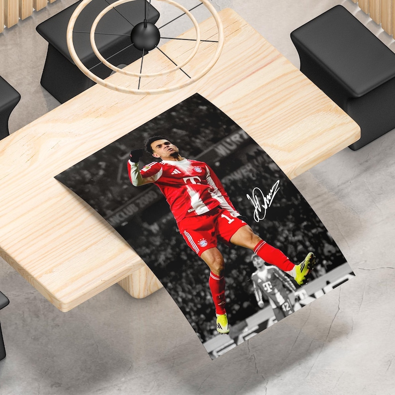 May include: A rectangular poster featuring a soccer player in a red and white jersey and shorts celebrating a goal. The background is a black and white stadium crowd scene. A white signature is printed on the right side of the image.