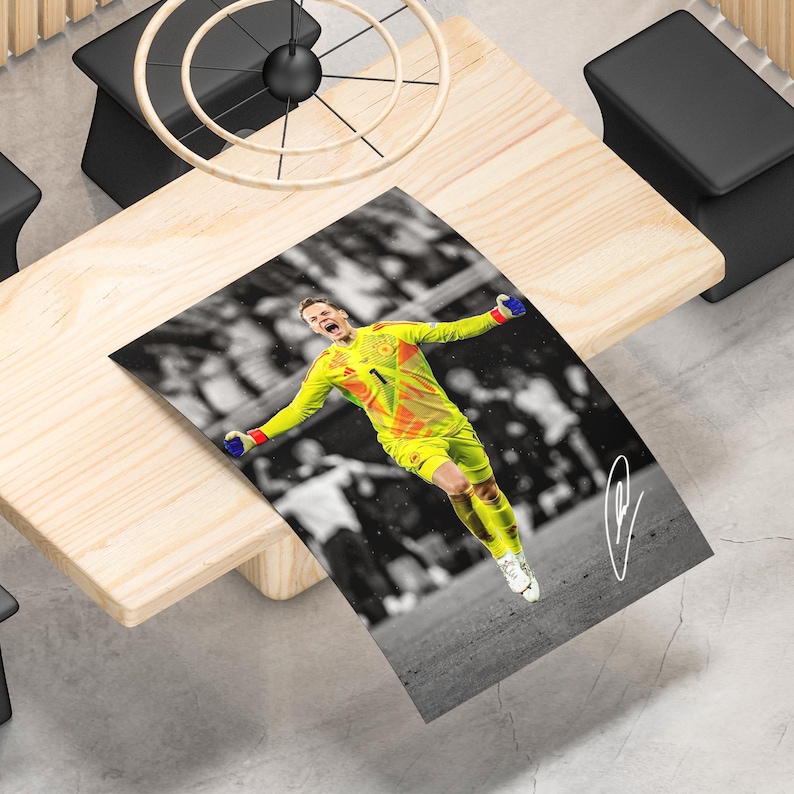 May include: A rectangular poster featuring a high-contrast action photograph of a soccer goalkeeper wearing a bright yellow and orange jersey with the number one, celebrating on a field with a blurred black and white crowd background and a white signature.