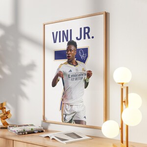 May include: A framed poster featuring soccer player Vini Jr. in a white jersey with the text "Emirates Fly Better." The poster includes the player's name and signature. The image is set against a white background.