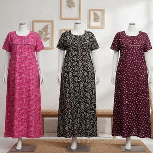 May include: Three long, short-sleeved nightgowns on mannequins. The gowns are in shades of pink, black, and burgundy. The pink gown has a white geometric pattern, the black gown has a paisley design, and the burgundy gown has white polka dots. The gowns are displayed on a neutral background.
