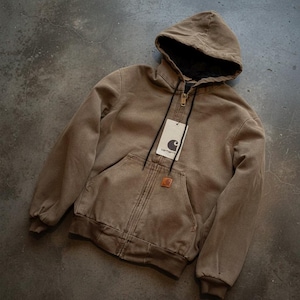 May include: A brown hooded jacket with a black interior lining and a front pocket. The jacket has a zip closure and a tag with a logo. The jacket is made of a durable material, suitable for outdoor wear.