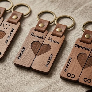 May include: Wooden keychains with a heart design. Each keychain has a leather strap and a metal ring. Some keychains have names and dates engraved, while others have hearts and dates. The keychains are made of wood and have a natural finish.