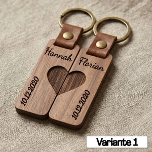 May include: Two wooden keychains with a heart-shaped cutout that forms a complete heart when placed together. Each keychain is engraved with a name and the date "10.12.2020". The keychains have brown leather straps and metal rings.