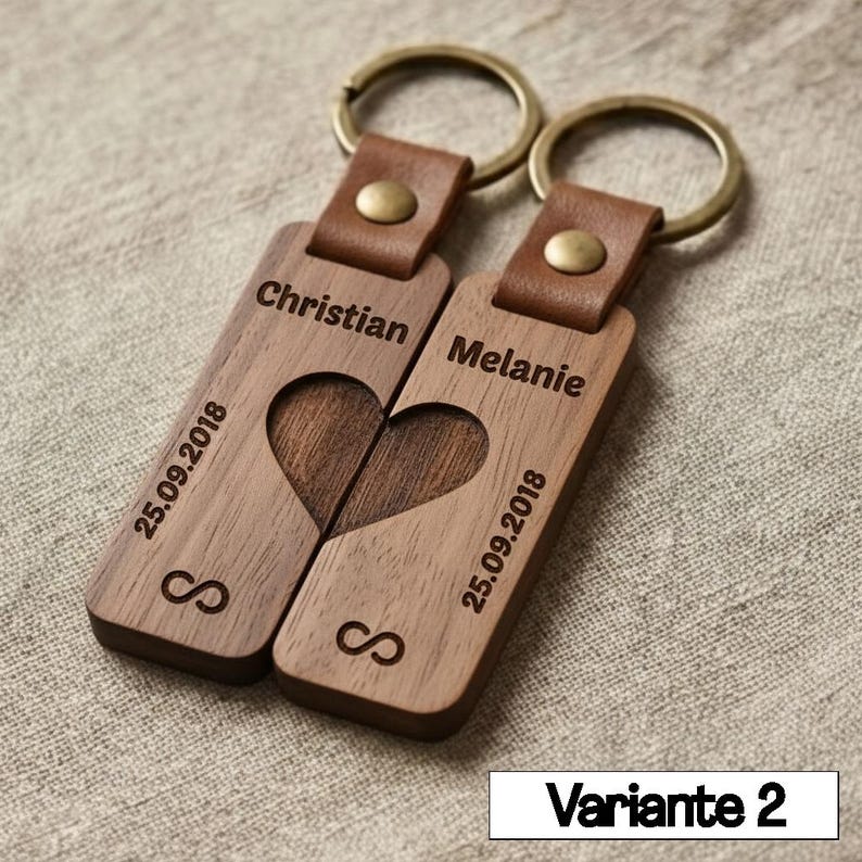 May include: Two wooden keychains with leather straps and metal rings. Each keychain is engraved with a name, date, and infinity symbol. The keychains, when placed together, form a heart shape.