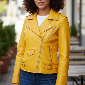 Puede incluir: Chaqueta de cuero amarilla brillante de estilo motero. Presenta cuello con solapas, bolsillos con cremallera y detalles plateados. La chaqueta tiene una silueta entallada y se combina con vaqueros azules. La chaqueta mide unos 50 cm.