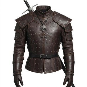 Puede incluir: Armadura de cuero marrón con detalles tachonados, cinturón negro y guantes a juego. Un colgante plateado cuelga del cuello. Una espada está colocada detrás de la armadura. La armadura tiene hombreras y está diseñada con múltiples paneles.
