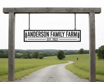 Puede incluir: Un letrero de metal negro para "Anderson Family Farm" colgado de un arco de madera. El letrero incluye espigas de trigo y el año de establecimiento, "Est. 2022". El letrero cuelga sobre un camino de grava que conduce a un campo verde.