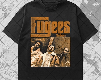 May include: Black t-shirt featuring a graphic of the hip-hop group Fugees. The design includes the band's name in a bold, orange font above a sepia-toned image of the group. The text "The Score" is below the band's name.