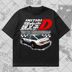 Könnte beinhalten: Schwarzes T-Shirt mit einer Grafik eines weiß-schwarzen Autos mit goldenen Felgen und japanischem Text. Der Text enthält "INITIAL D" in Weiß und Rot sowie zusätzlichen japanischen Text.