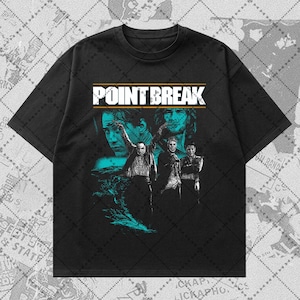 Puede incluir: Camiseta negra con un gráfico de la película "Point Break". El diseño incluye el título de la película en blanco y dorado, junto con imágenes de los actores. La obra de arte tiene una combinación de colores turquesa y blanco.