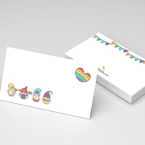 May include: White envelopes with colorful illustrations. One envelope features a rainbow heart and a row of cartoon gnomes. Another stack of envelopes has a banner of colorful flags. The envelopes are on a light gray surface.