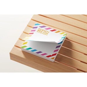 May include: A white notepad with the text "Closets are for Clothes" in gold lettering. The notepad has a rainbow-colored diagonal stripe border. The notepad is on a wooden surface.