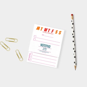 May include: A white notepad with a colorful "MTWTFSS" heading and the text "Notepad 50 Pages 4.25" x 5.5" printed on the front. The notepad is sitting on a white surface with three gold paper clips and a black and white polka dot pencil.