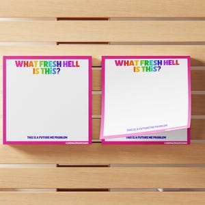 May include: Two pink-framed notepads with the text "WHAT FRESH HELL IS THIS?" in rainbow colours. The bottom of the notepad reads "THIS IS A FUTURE ME PROBLEM". The notepads are on a wooden surface.