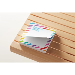 May include: A white notepad with a rainbow diagonal stripe design and the text "EQUALITY HURTS NO ONE." The notepad is on a wooden surface. The notepad's design includes red, orange, yellow, green, blue, and purple colors.