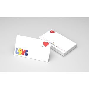 May include: White stationery cards with colorful "LOVE" text and a red heart pierced by an arrow. A stack of cards features a heart design and a decorative border of hearts and arrows. Stationery for Valentine's Day or romantic occasions.