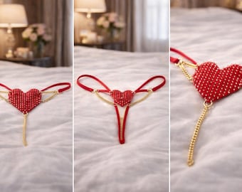 May include: Red heart-shaped lingerie with a beaded surface and gold-coloured chain accents. The lingerie features a thong design with a heart-shaped centrepiece and dangling chain.